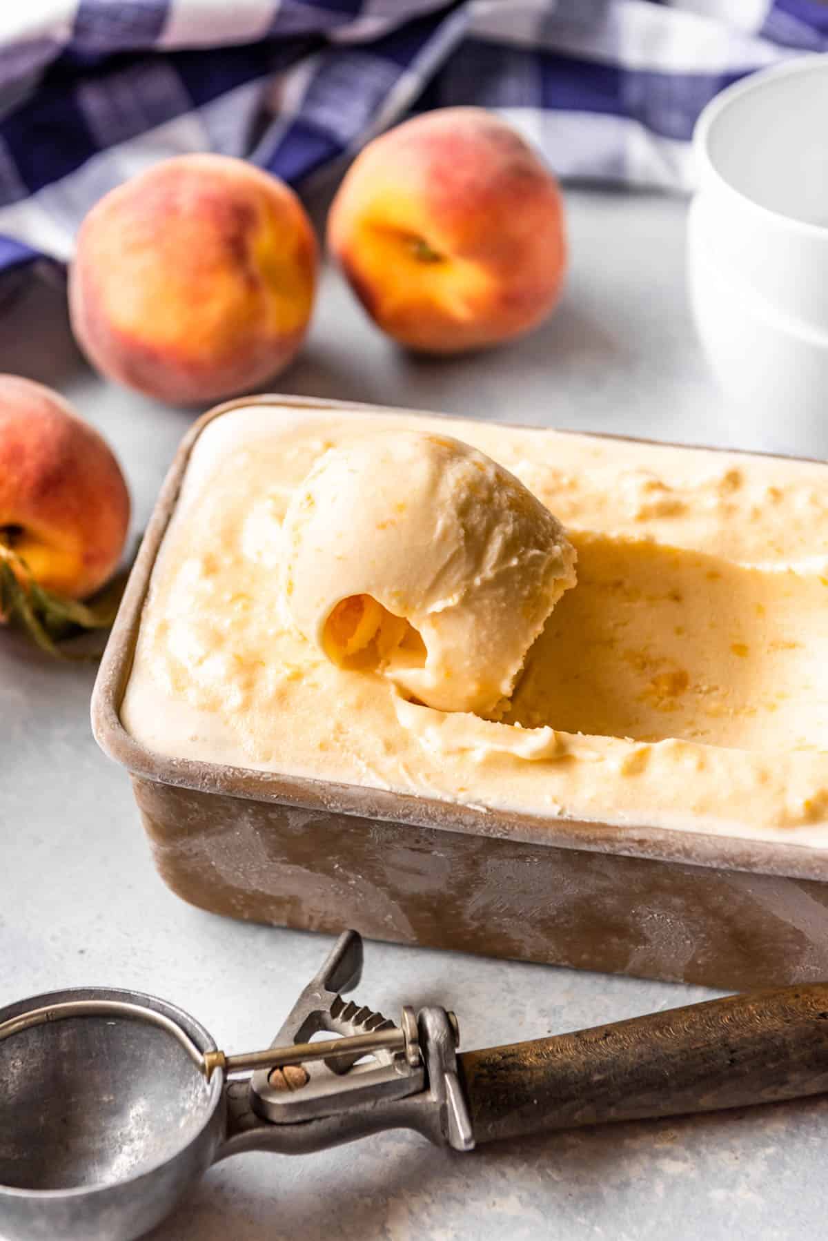 A scoop of fresh peach icecream in a loafpan with a curled scoop and a scooper off to the side.