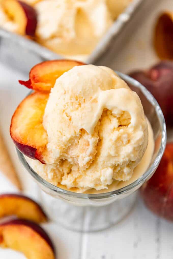 A glass bowl of homemade peach ice cream with slices of fresh peaches in it.