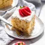 A slice of homemade tres leches cake on a white plate with a fanned strawberry on top.