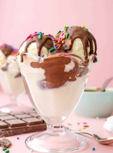 An ice cream sundae glass with scoops of vanilla ice cream topped with chocolate magic shell and sprinkles.