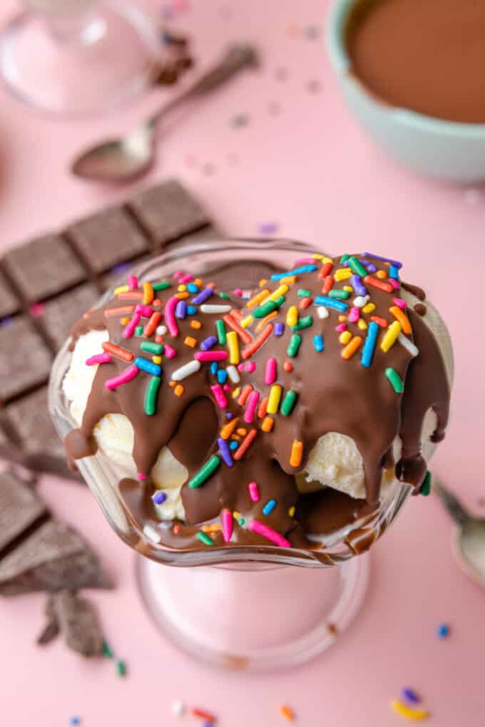 Hardened chocolate magic shell topping with sprinkles over scoops of vanilla ice cream in a bowl next to chocolate bars.