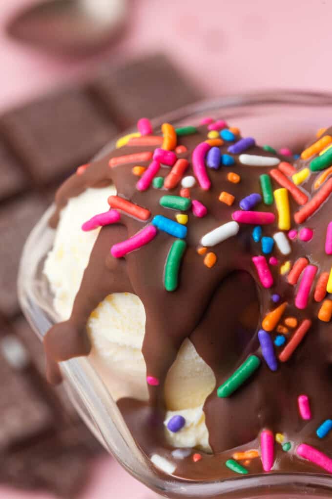 Hardened chocolate magic shell topping with sprinkles over scoops of vanilla ice cream in a bowl.