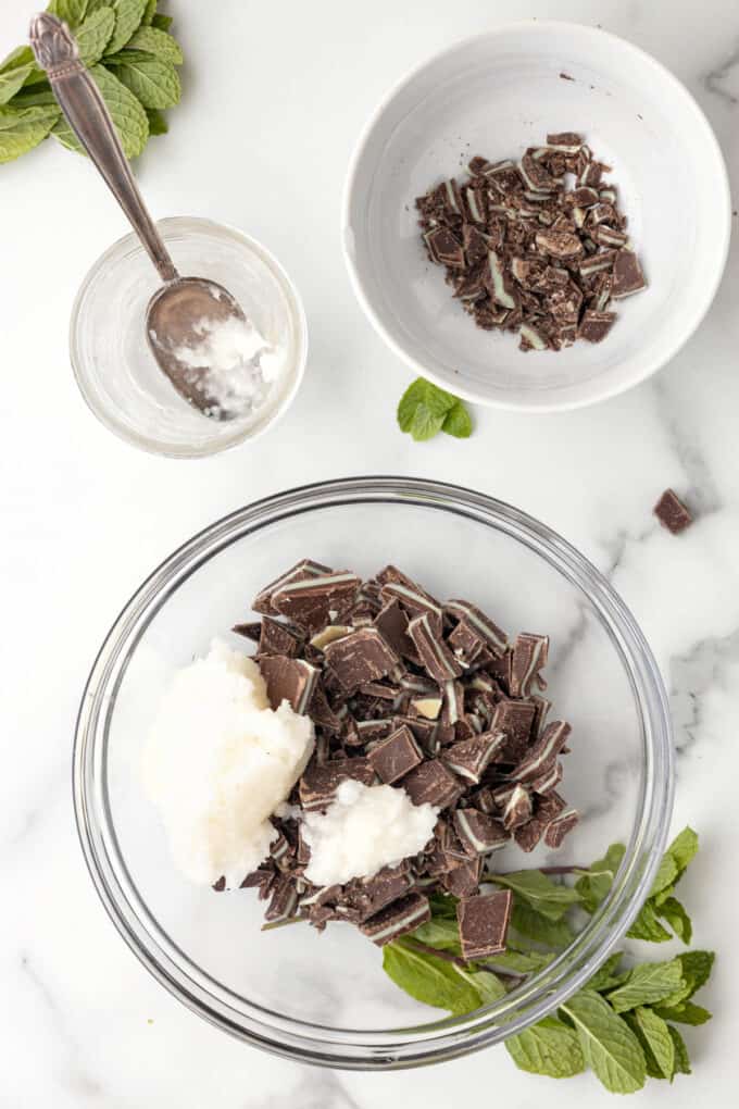 Adding coconut oil to a bowl of chopped Andes mints.