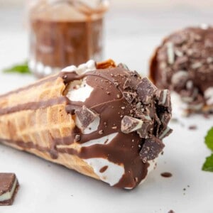 An ice cream cone with mint chocolate magic shell topping in front of a jar of magic shell.
