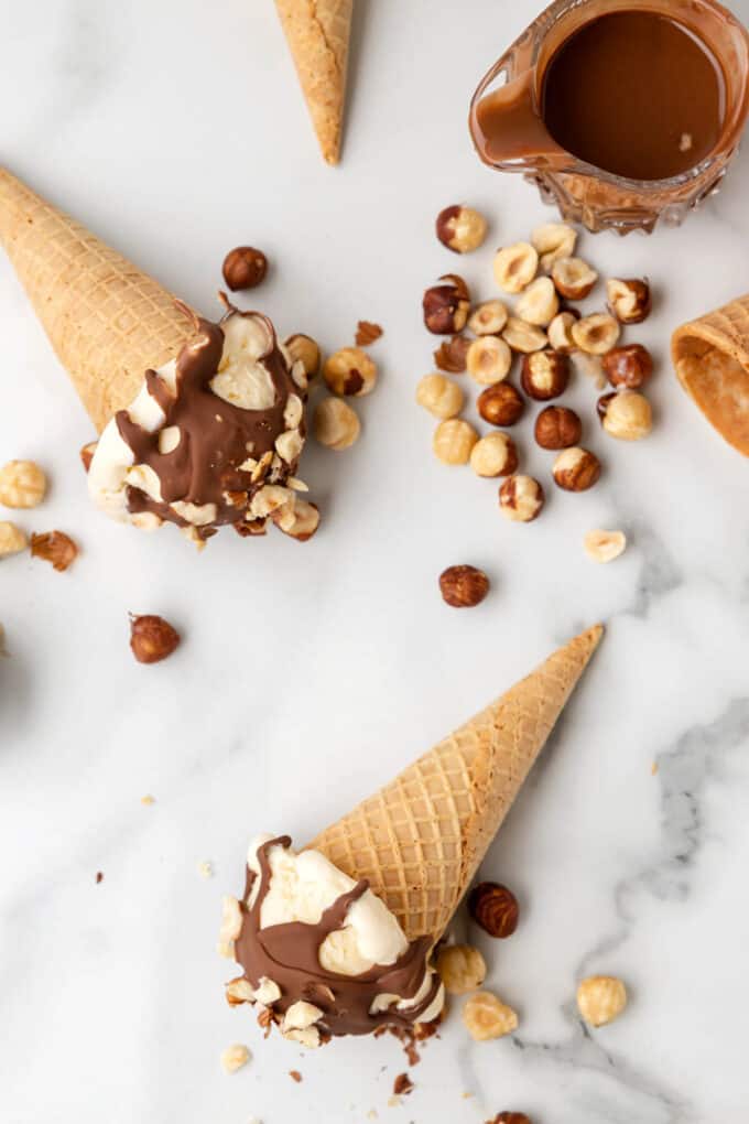 Ice cream cones with Nutella magic shell laying on their sides with hazelnuts around them.