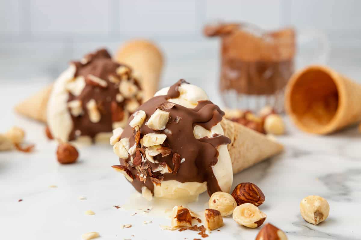 Ice cream cones with vanilla ice cream topped with Nutella magic shell and chopped hazelnuts.