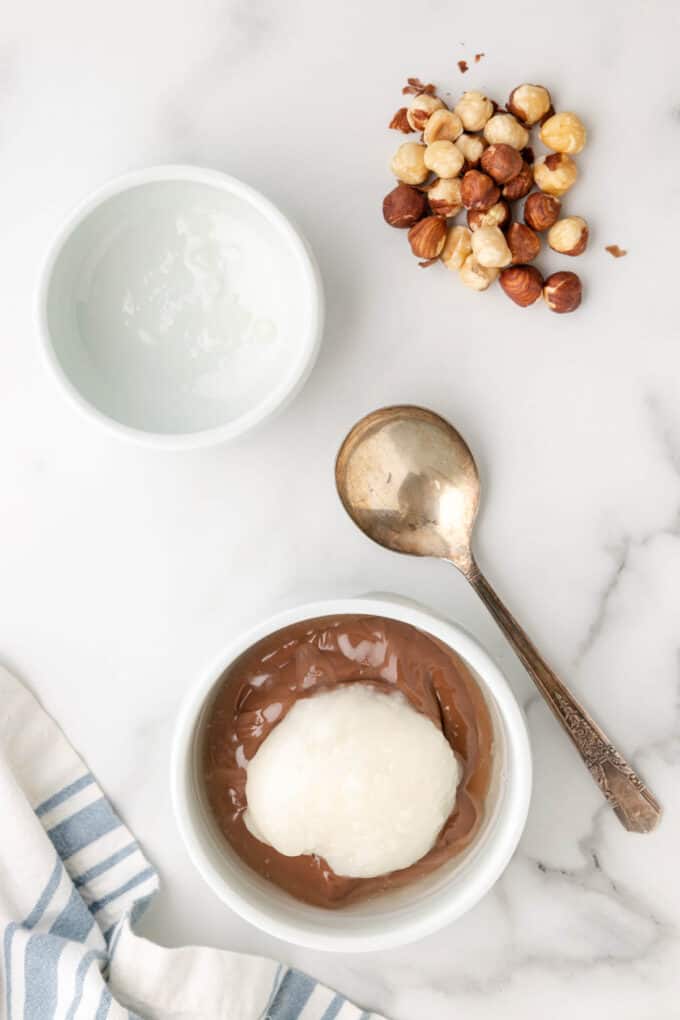 Coconut oil being added to a bowl of chocolate hazelnut spread.