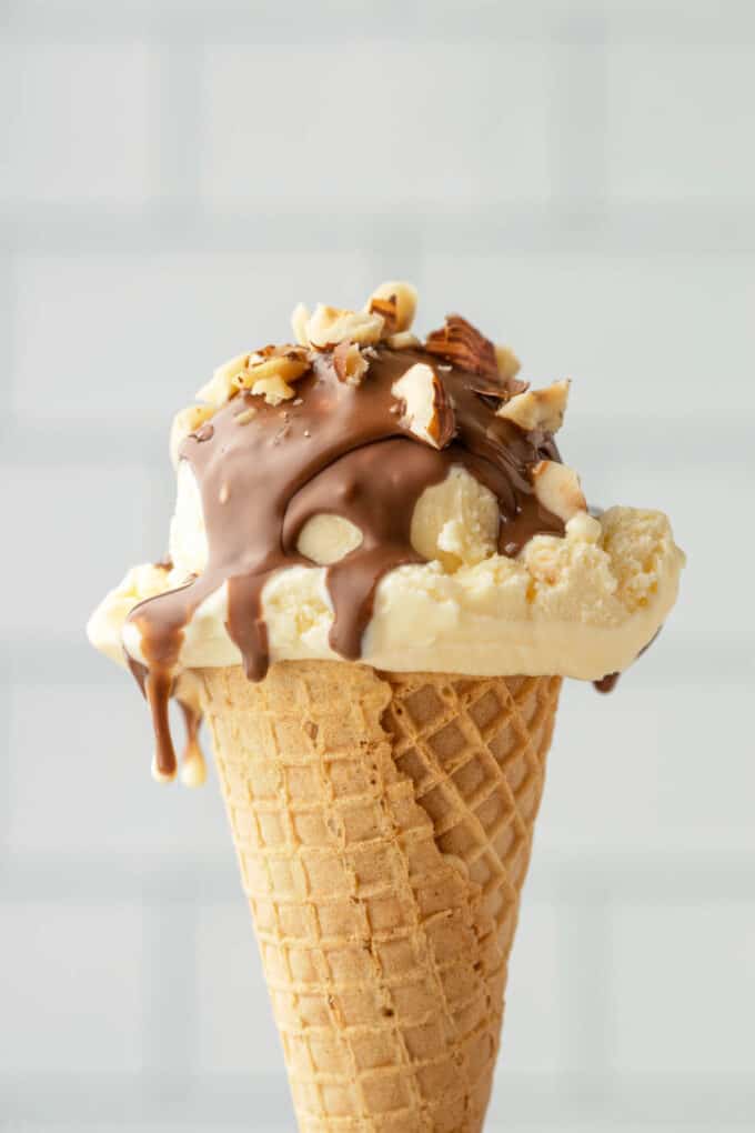 A scoop of vanilla ice cream covered in Nutella magic shell and chopped hazelnuts on a sugar cone.