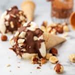 An ice cream cone lying on its side with Nutella magic shell and chopped hazelnuts on top.