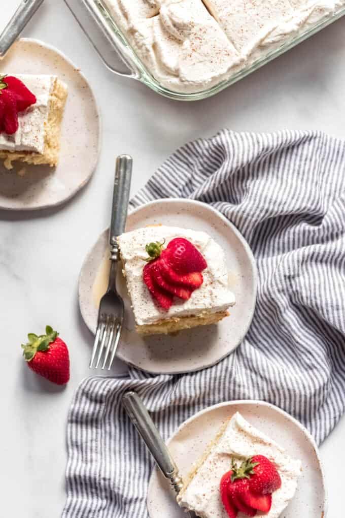An aerial view of sliced tres leches cake on white plates with strawberries and in a baking dish.