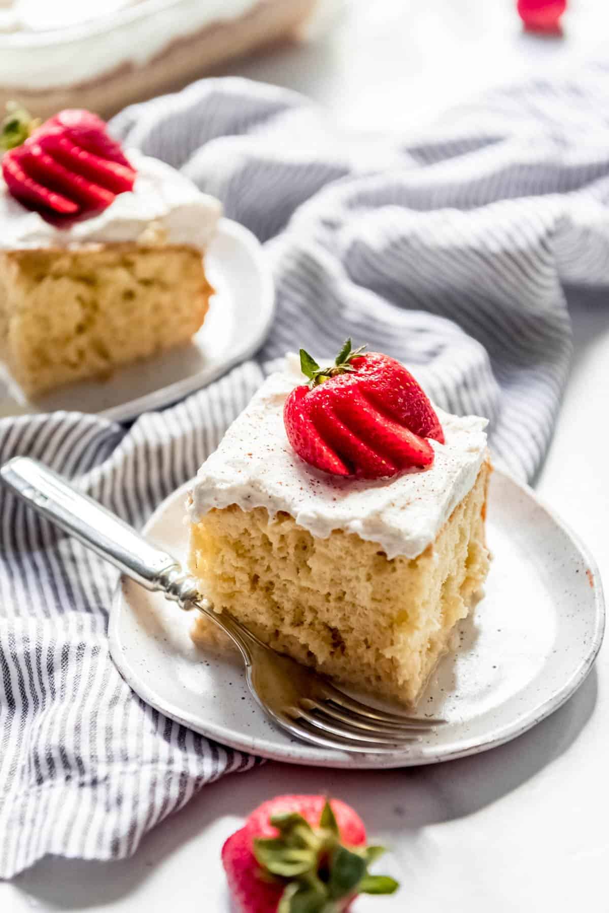Sliced and frosted squares of tres leches cake on plates with fanned strawberries as garnish on top.