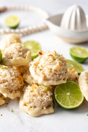 Coconut Lime Macaroons dipped in chocolate next to limes and a juice.