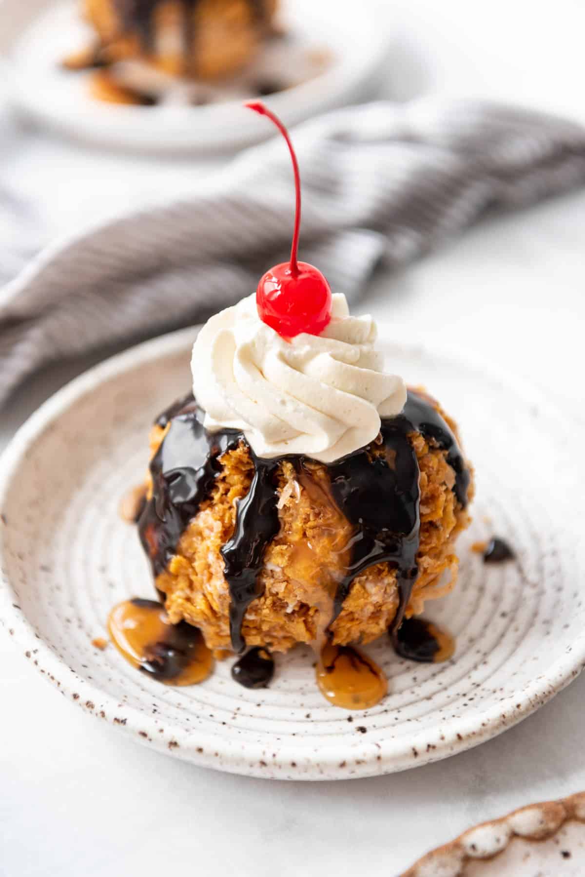 Homemade easy fried ice cream on a plate with chocolate sauce, whipped cream, and a cherry.