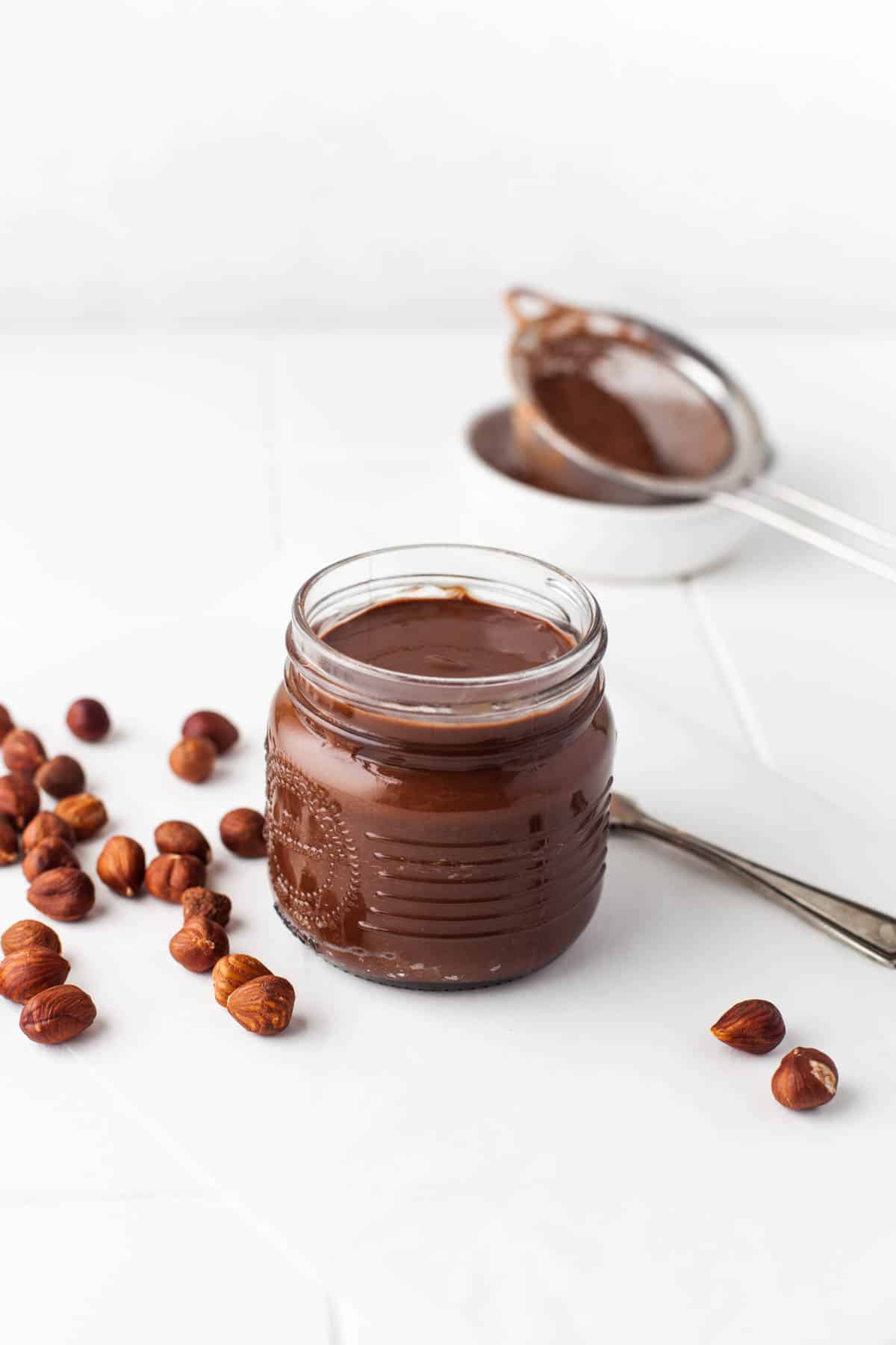 Whole toasted hazelnuts next to a jar of Homemade Nutella.