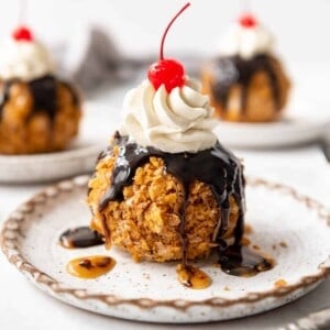 A Mexican fried ice cream ball with chocolate and caramel syrup, whipped cream, and a cherry on a plate.