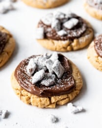 Close up view of Crumbl copycat muddy buddy cookies with Chex Mix muddy buddies on top, on a white surface.