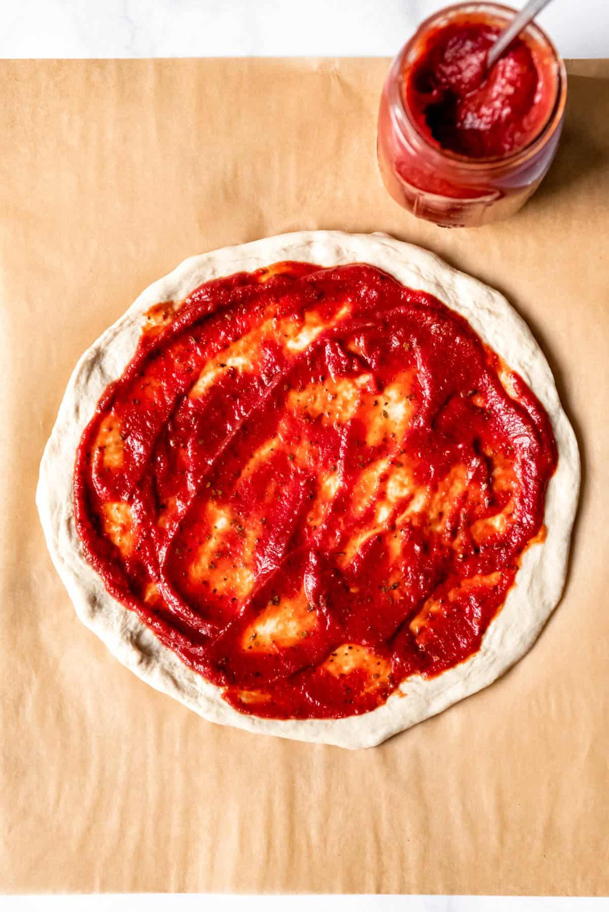 An image of pizza dough topped with homemade pizza sauce.