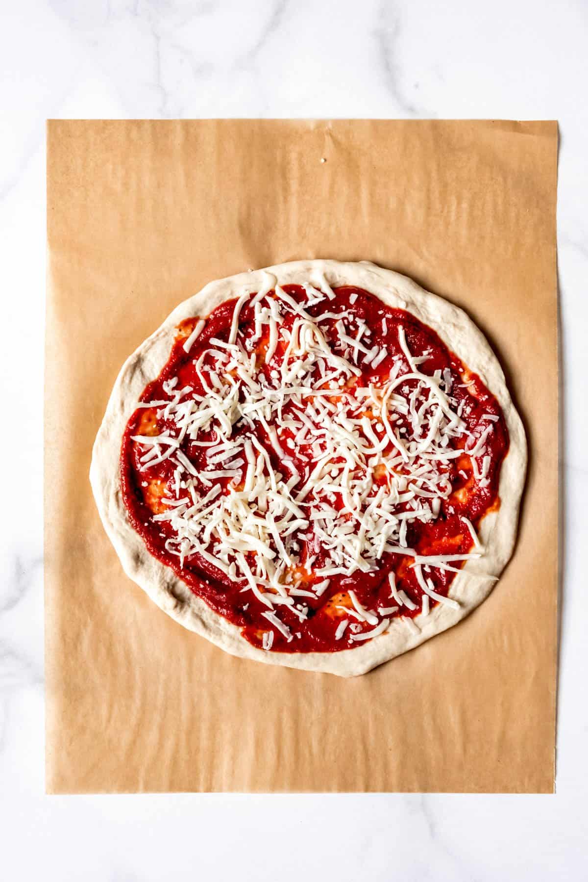 Sprinkling grated mozzarella cheese onto a pizza topped with sauce.