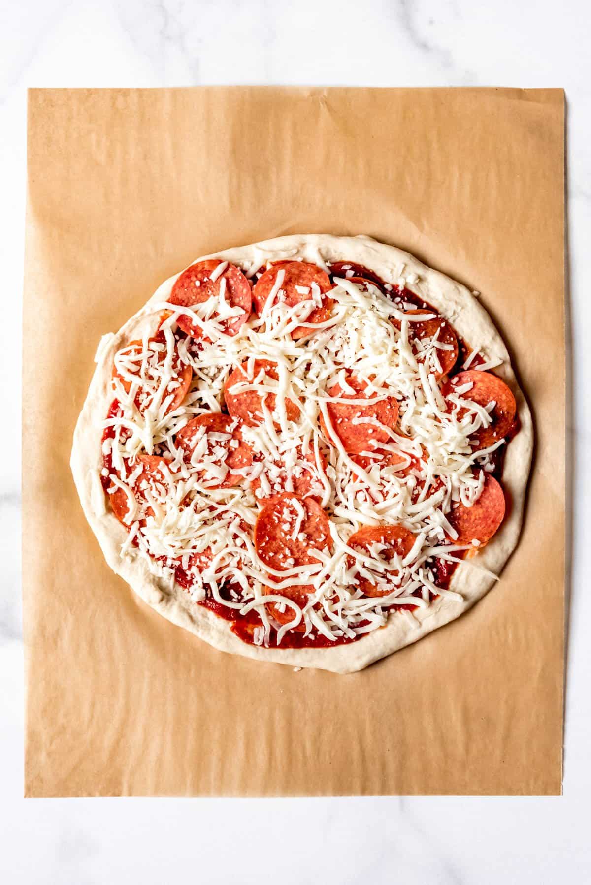 Sprinkled mozzarella cheese over pepperoni pizza before baking.