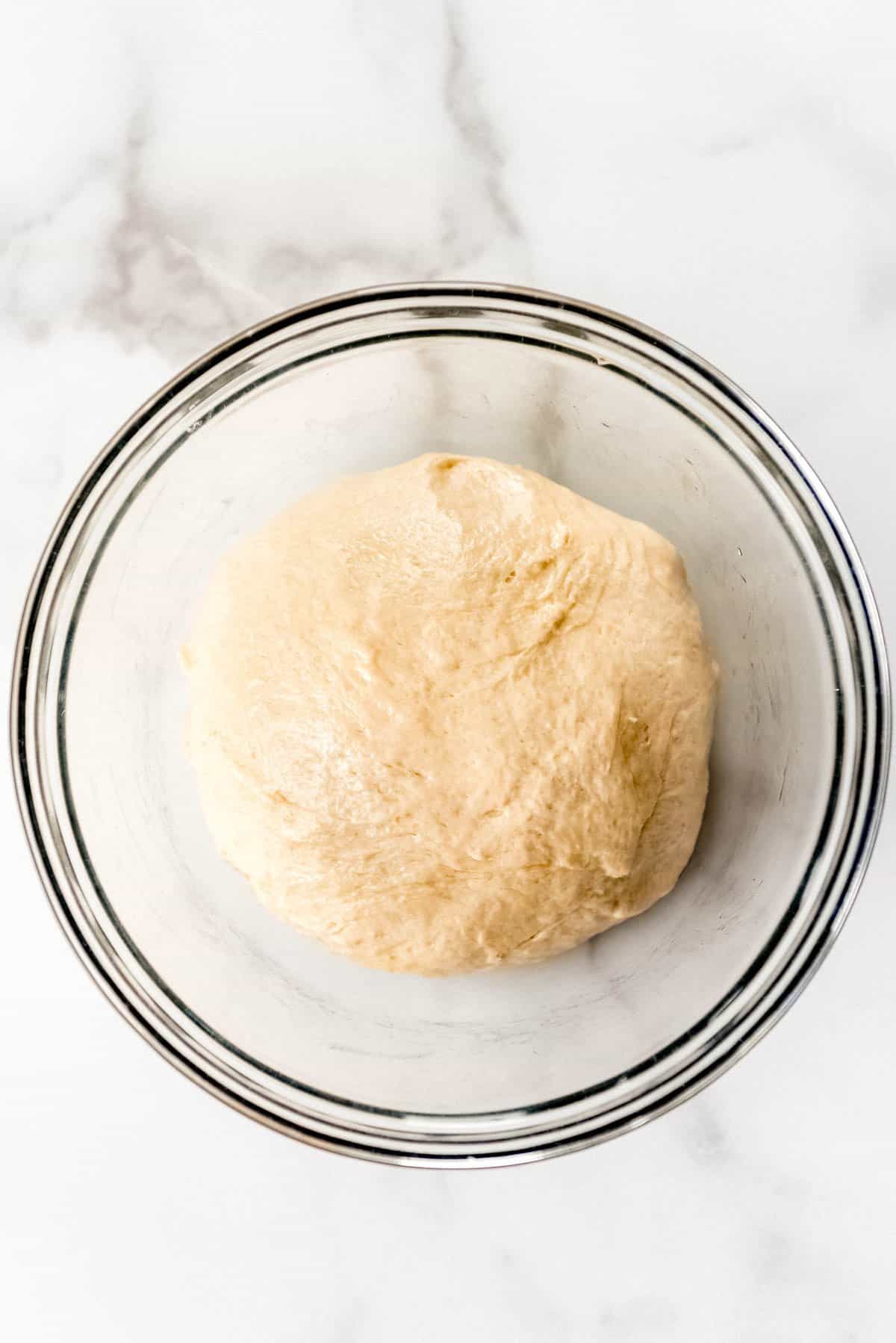 A ball of homemade pizza dough in an oiled glass bowl.