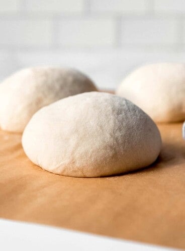 An image of balls of homemade pizza dough on parchment paper.