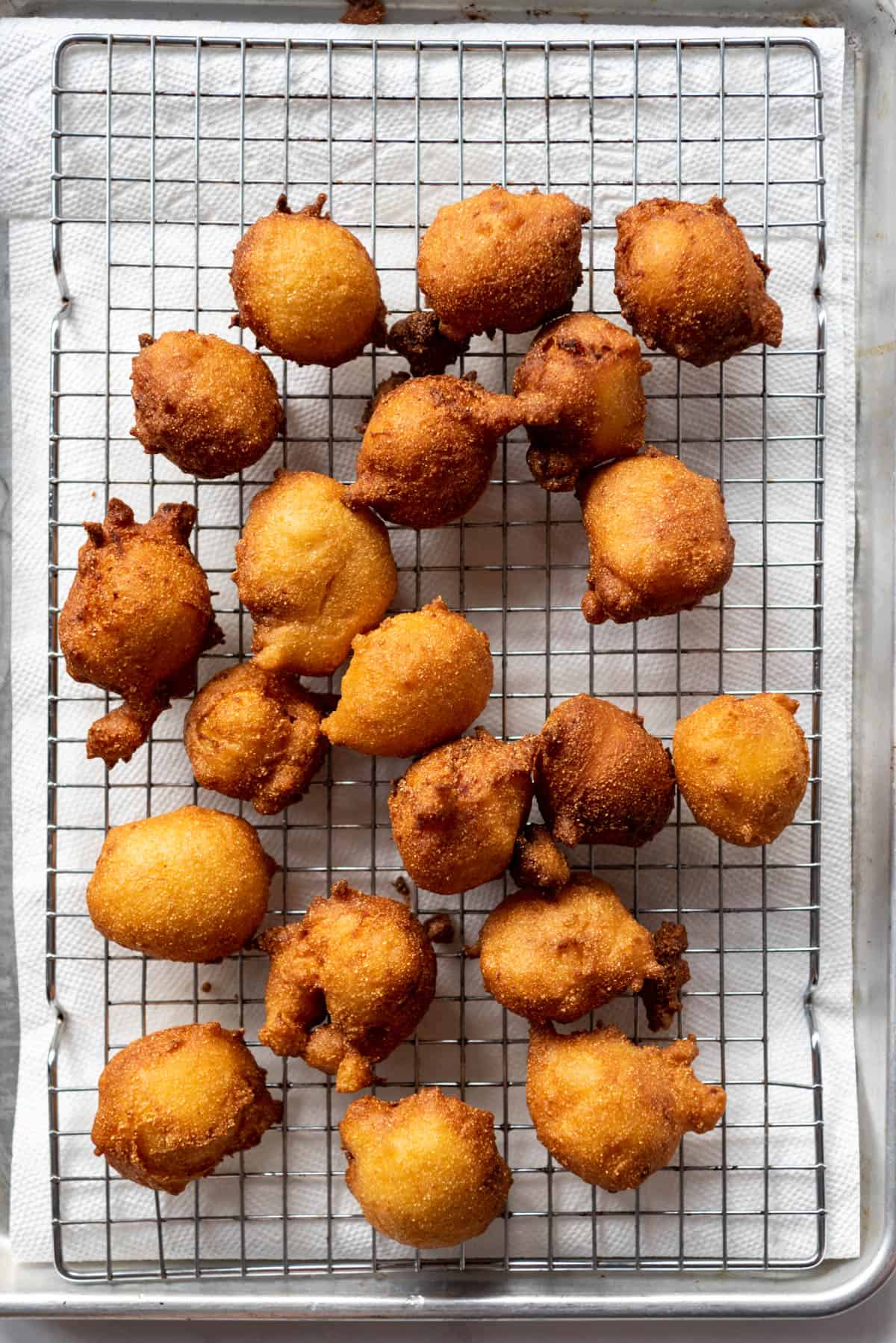 Freshly fried hush puppies draining on a wire rack over paper towels.