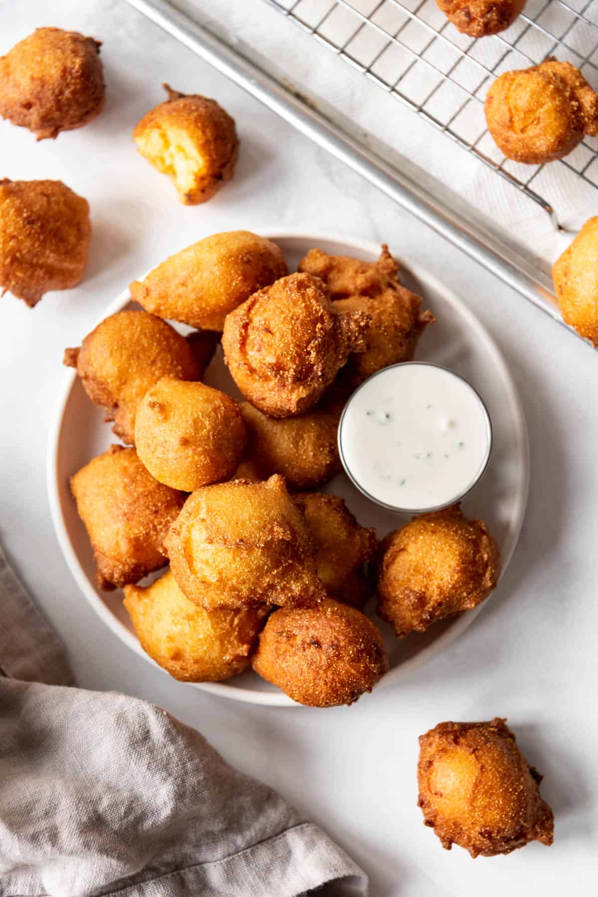 A plate of golden brown hush puppies with ranch dipping sauce.