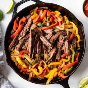 Grilled steak fajitas filling with peppers and onions in a cast iron skillet.