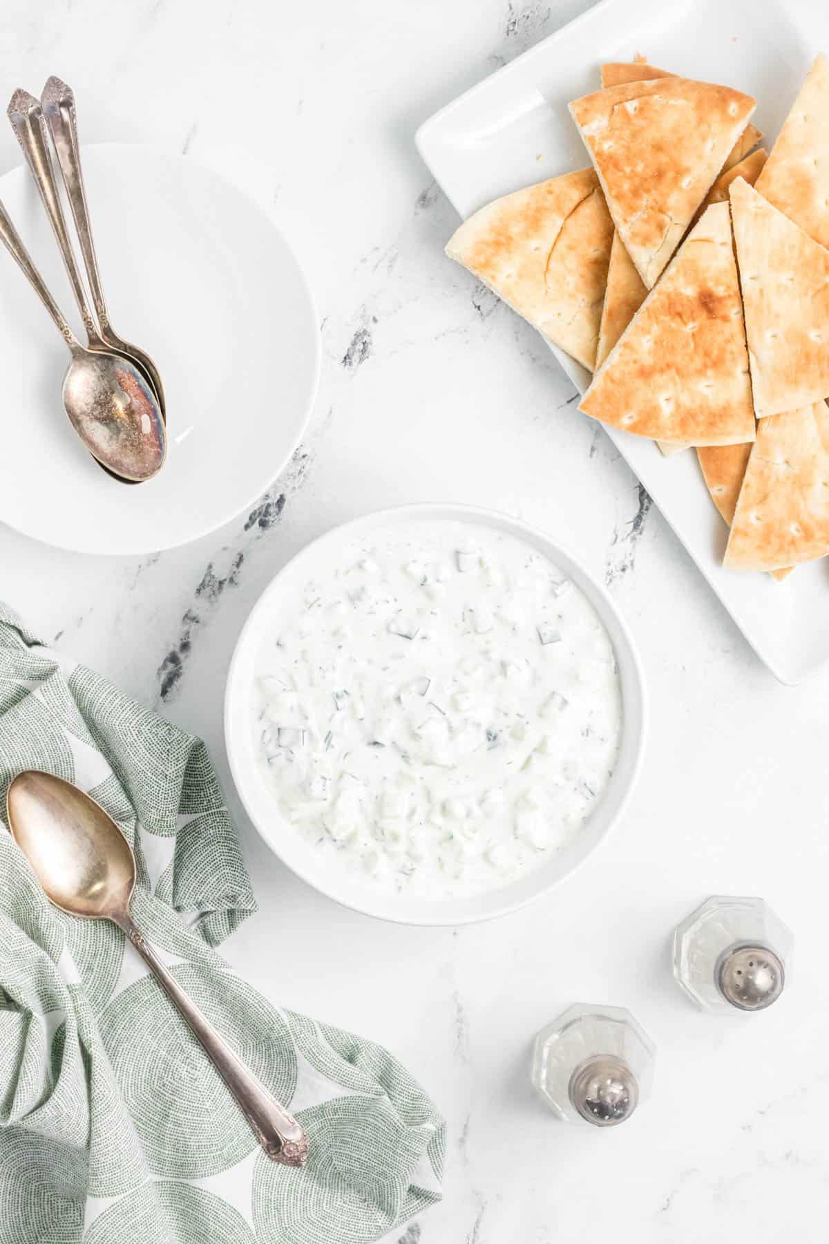 A bowl of tzatziki sauce next to a plate of pita bread cut into triangles.