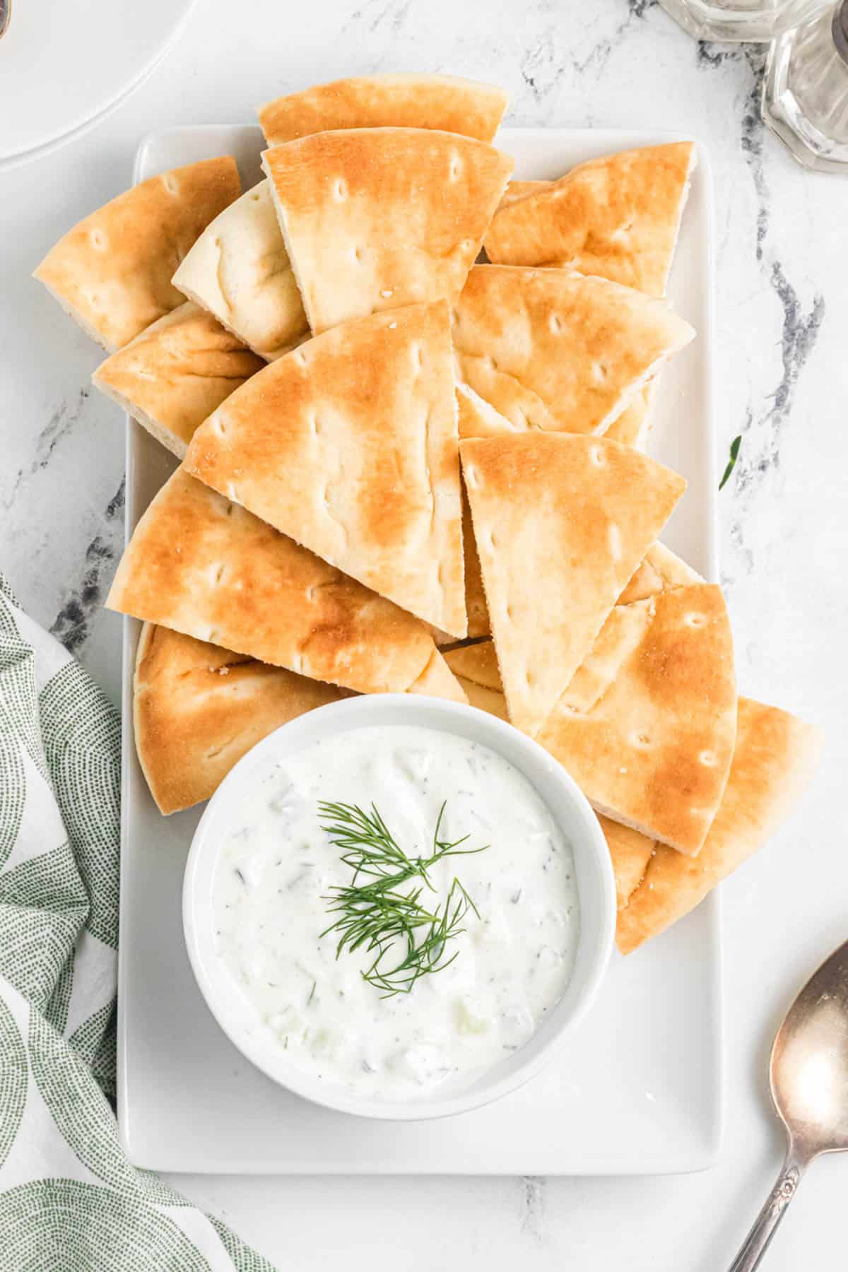 A serving platter with a bowl of tzatziki sauce for dipping and soft pita bread wedges.