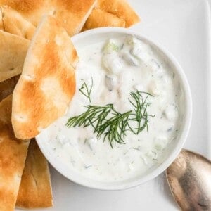 A bowl of tzatziki sauce with fresh dill and pita bread.