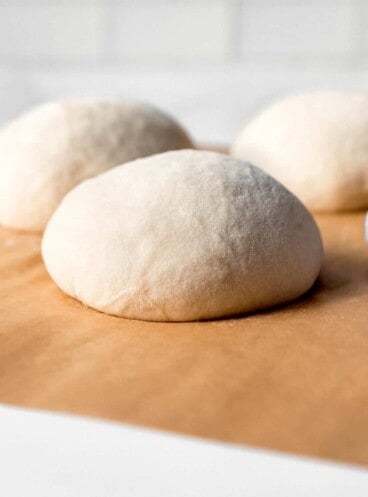 An image of balls of homemade pizza dough on parchment paper.