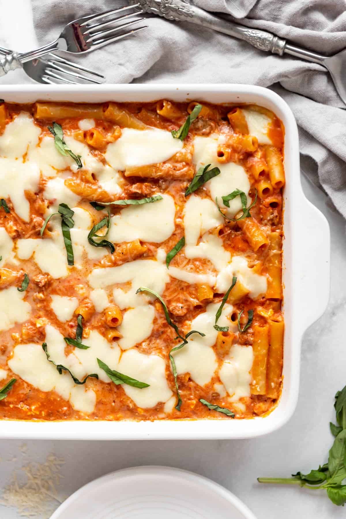 An overhead image of baked ziti in a casserole dish with fresh basil sprinkled on top.
