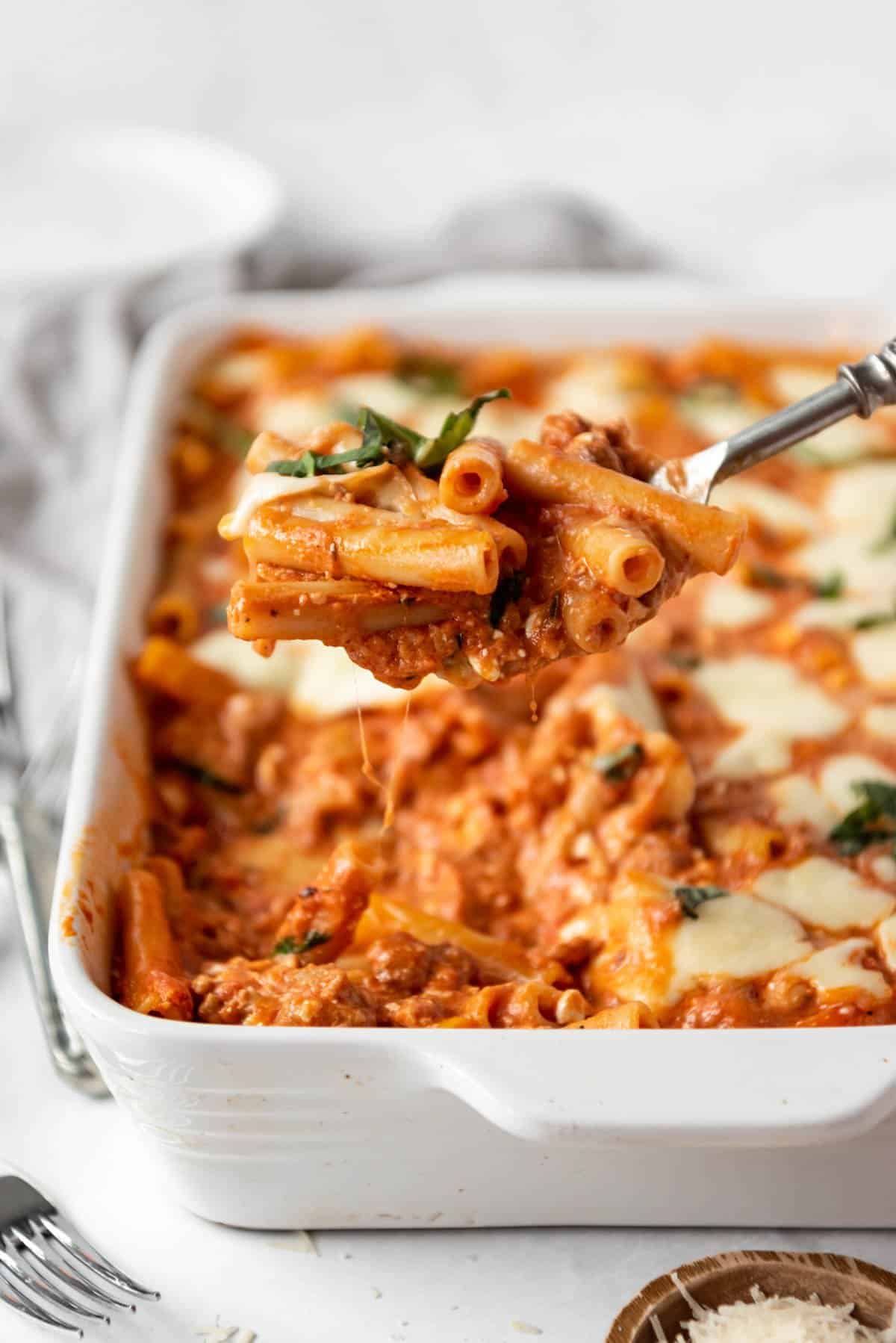 A spoonful of baked ziti being lifted out of the pan.