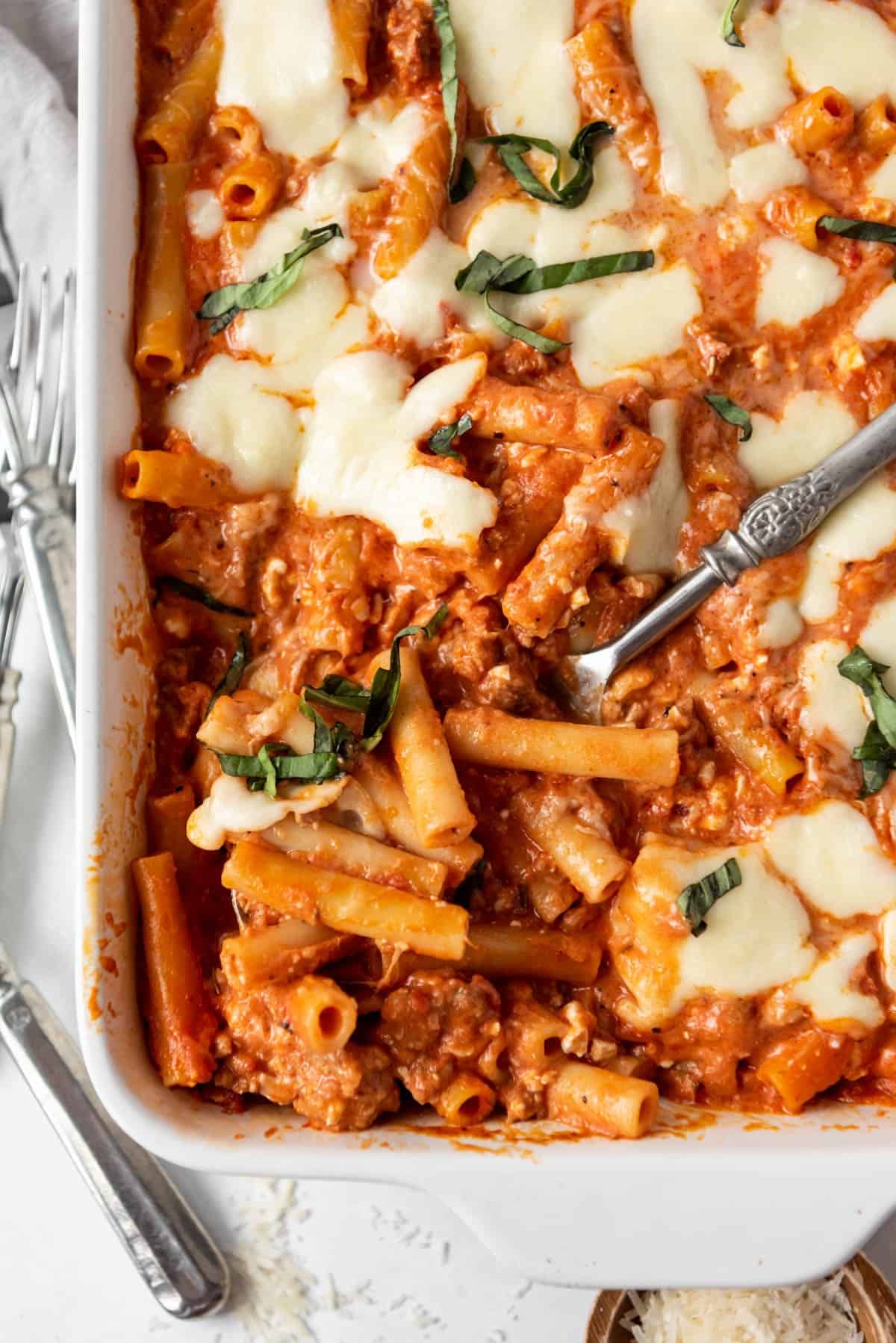 A serving spoon in a white casserole dish of baked ziti.