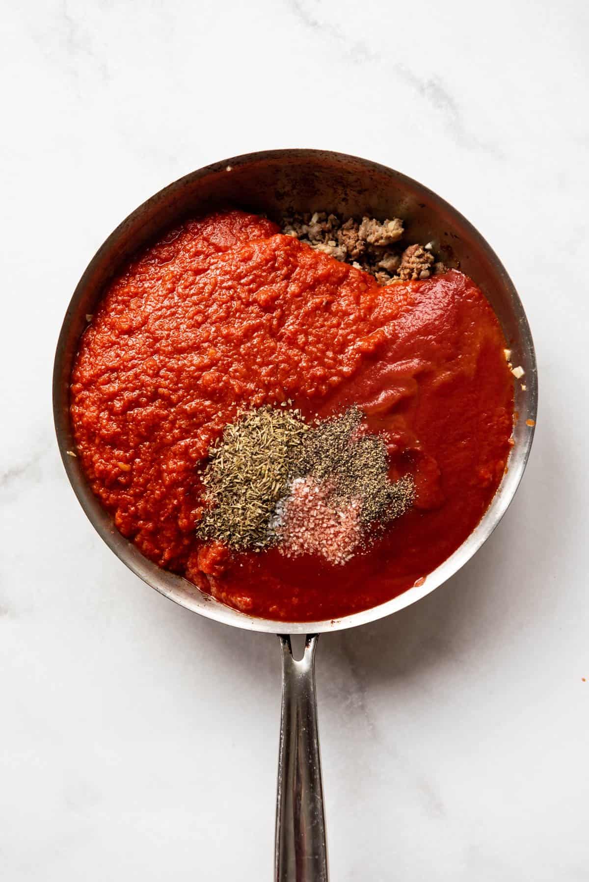 Adding marinara sauce, tomato sauce, and seasonings to browned Italian sausage in a large skillet.