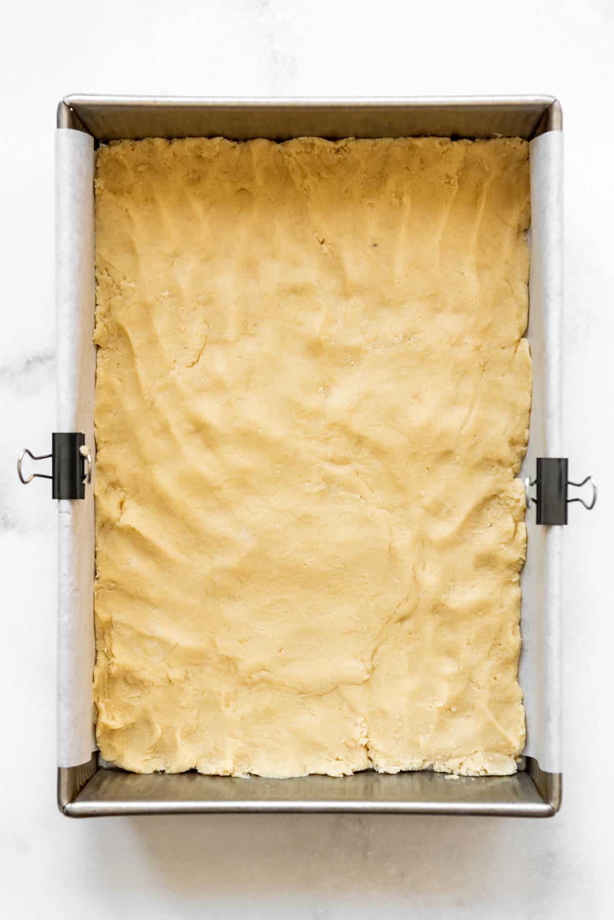 Pressing a shortbread crust into the bottom of a 9x13-inch baking dish.