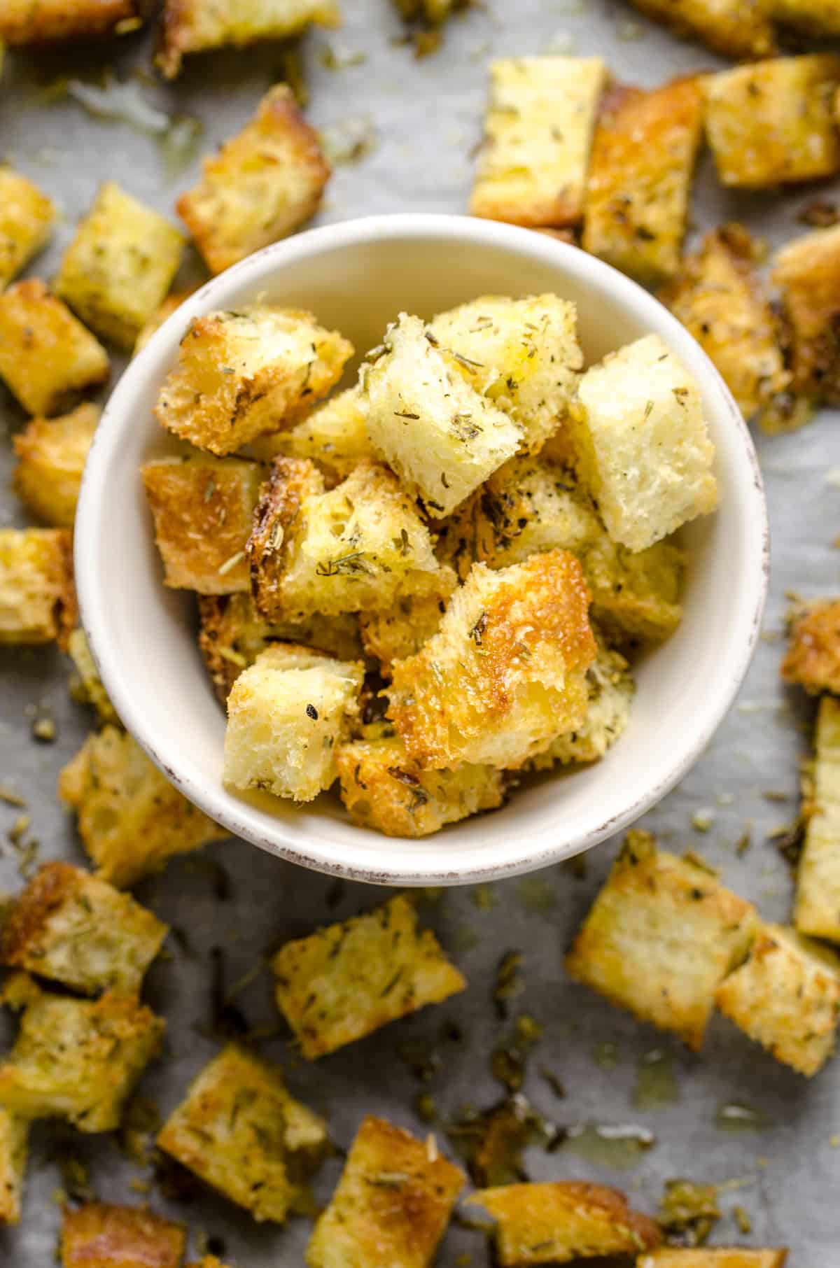 A bowl of homemade croutons on top of a piece of parchment paper holding additional croutons