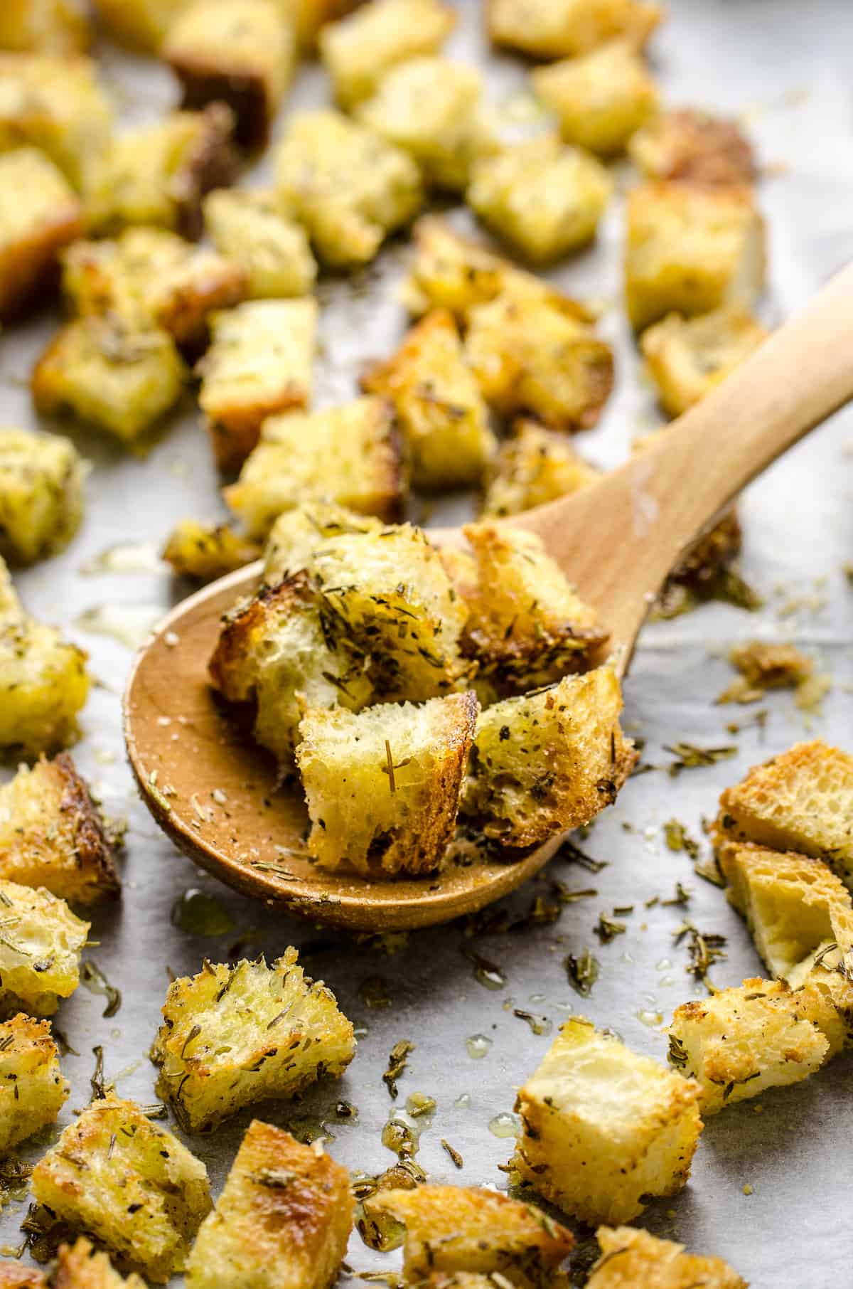 Six homemade croutons on a wooden spoon with more croutons surrounding it