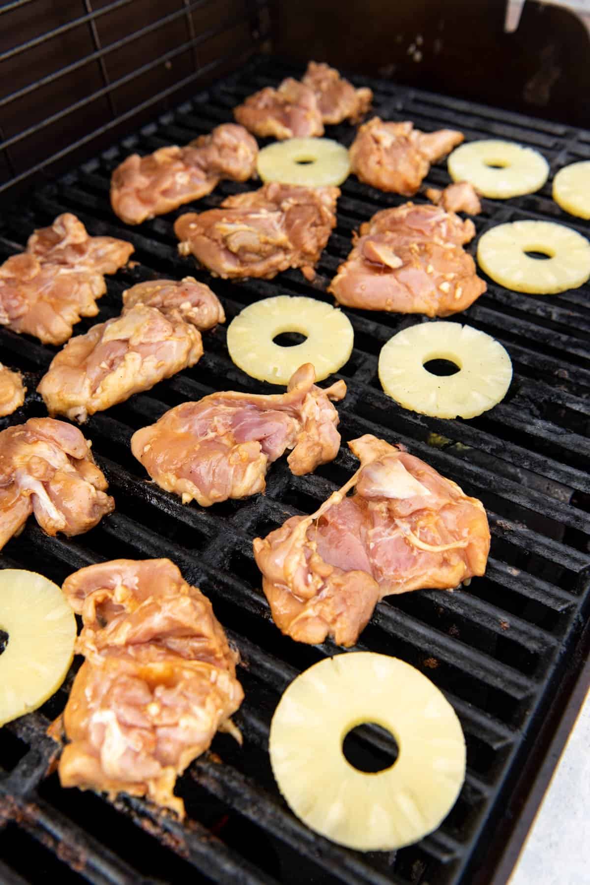 Boneless, skinless chicken thighs on the grill with pineapple rings.