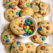 A batch of M&M cookies on a serving platter along with a bowl of M&Ms