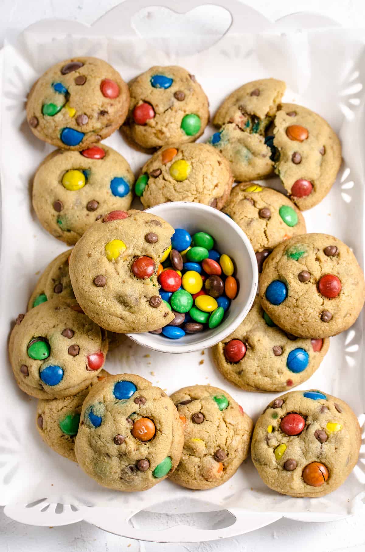 A batch of M&M cookies on a serving platter along with a bowl of M&Ms