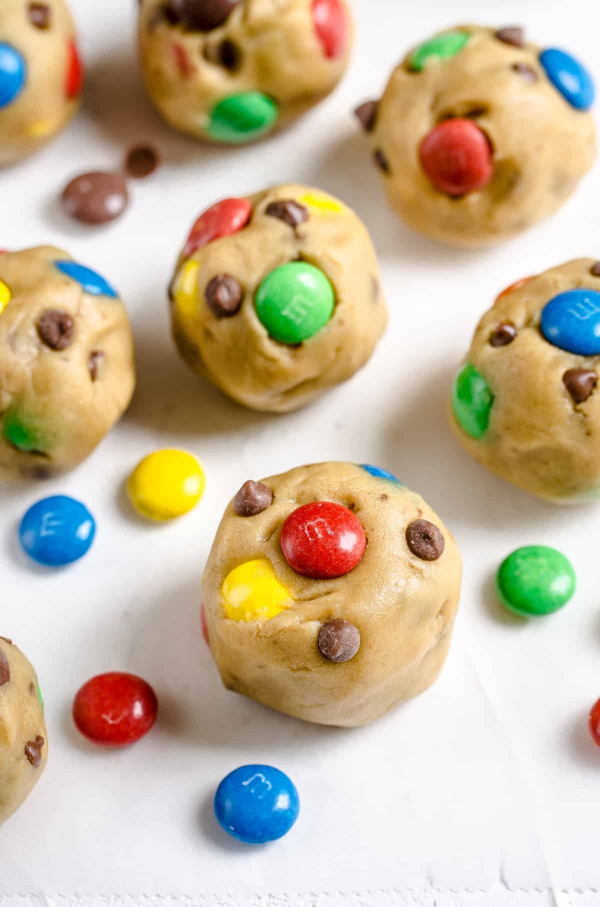 A close-up shot of unbaked balls of cookie dough on top of a sheet of parchment paper