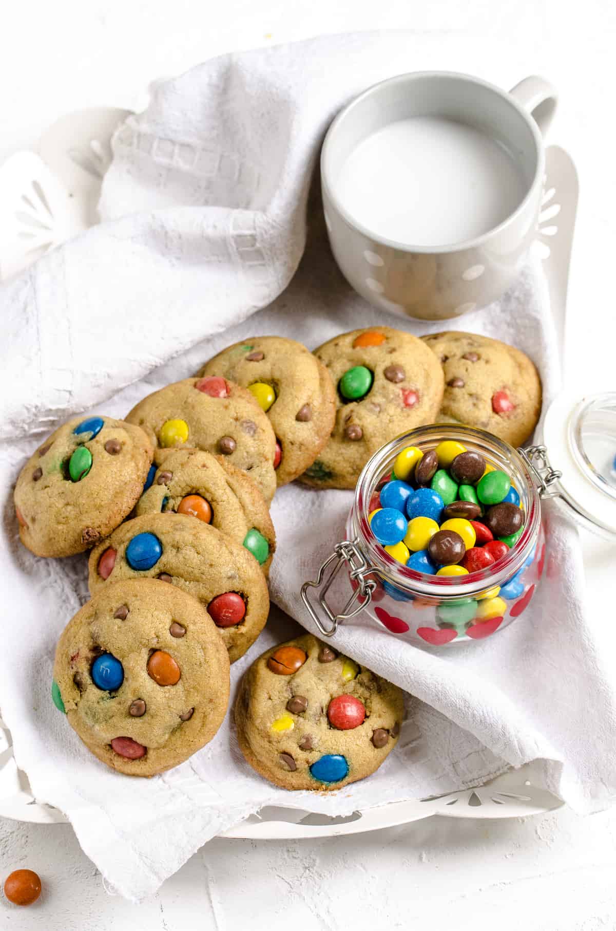 A serving platter holding homemade cookies, a jar of M&Ms and a glass of milk