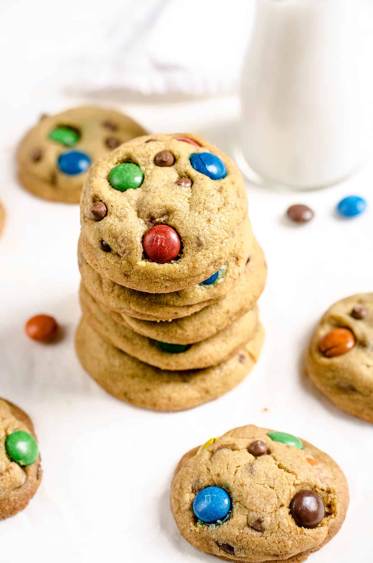 Six M&M cookies stacked on top of each other with a few loose cookies beside the stack