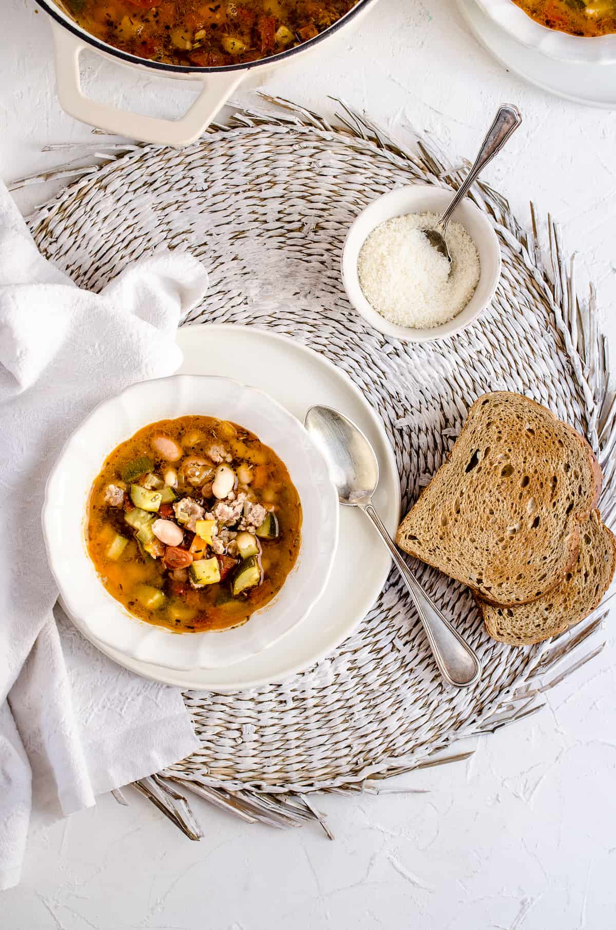 An overhead shot of a bowl of minestrone soup beside a white dishtowel