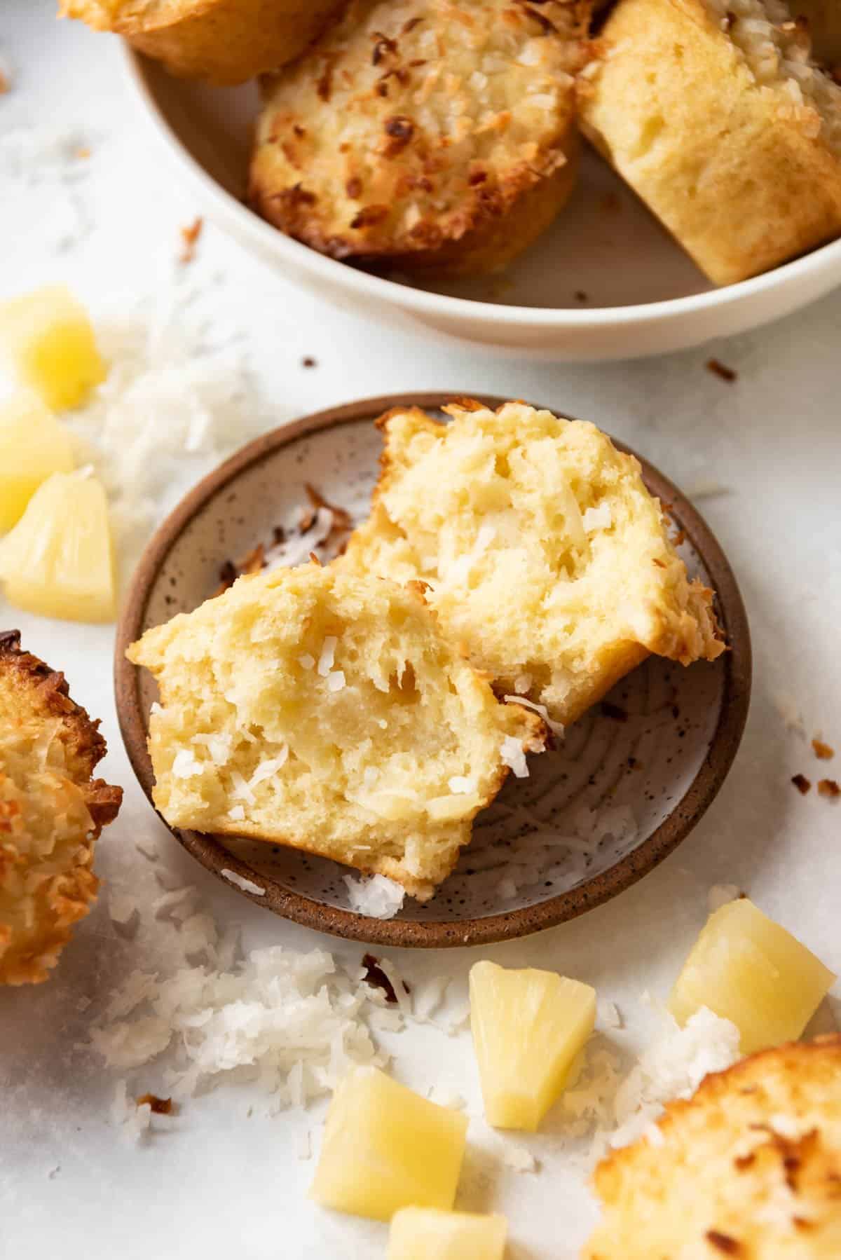 The soft, fluffy interior of a pineapple coconut muffin on a plate next to pineapple and coconut.