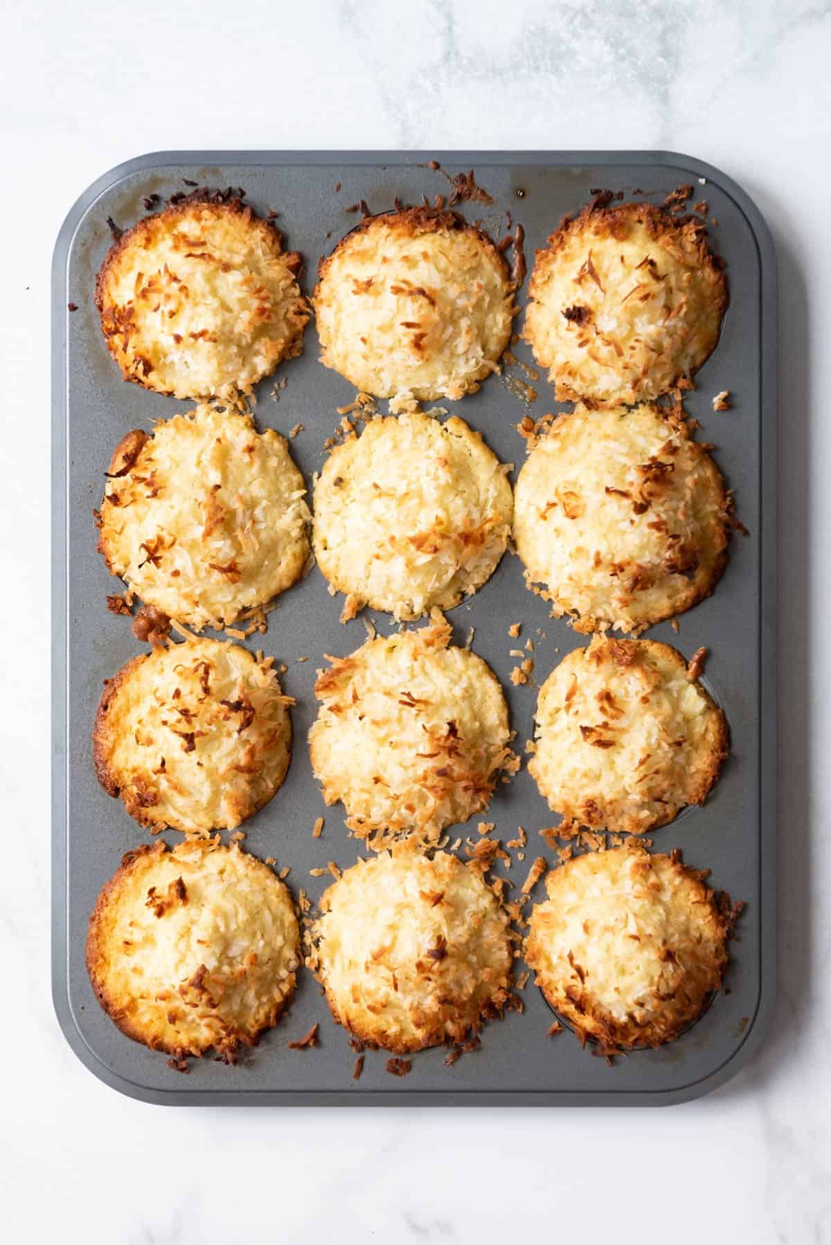 A dozen baked muffins with toasted coconut on top.