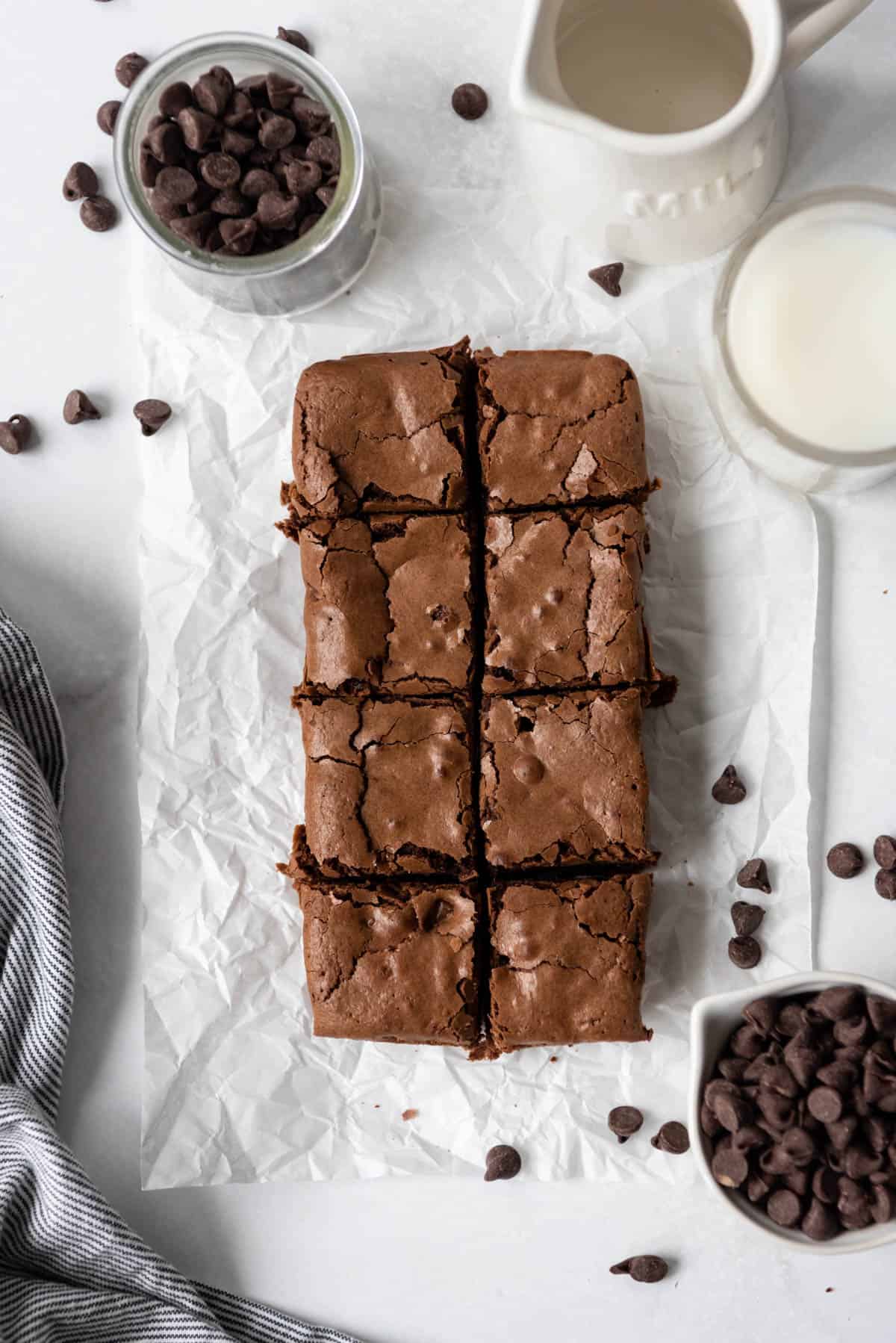 A small batch of chocolate brownies cut into eight small squares next to chocolate chips and a glass of milk.