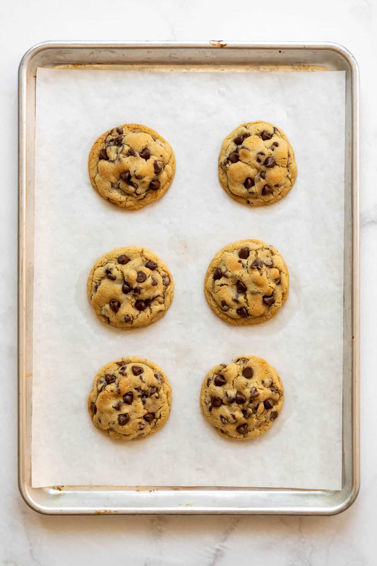 Six small batch chocolate chip cookies on a baking sheet.